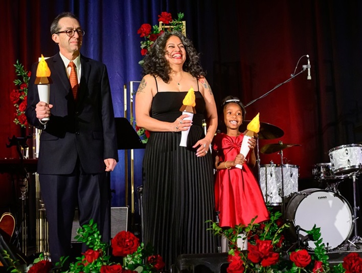 Man, woman, and child standing on stage holding up lit torches.